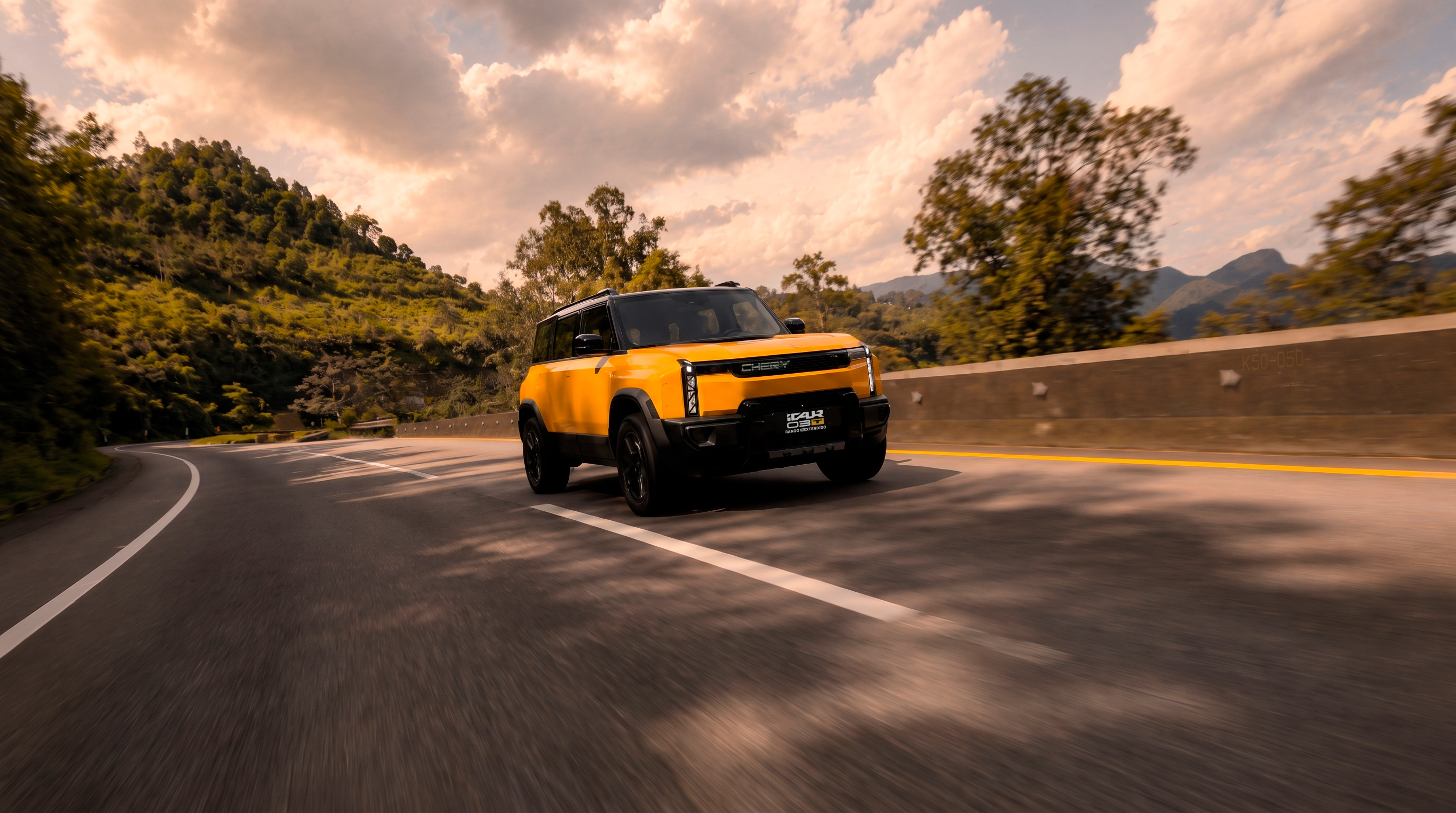 Chery iCAR 03T amarillo de rango extendido recorriendo una carretera de montaña con cielo nublado